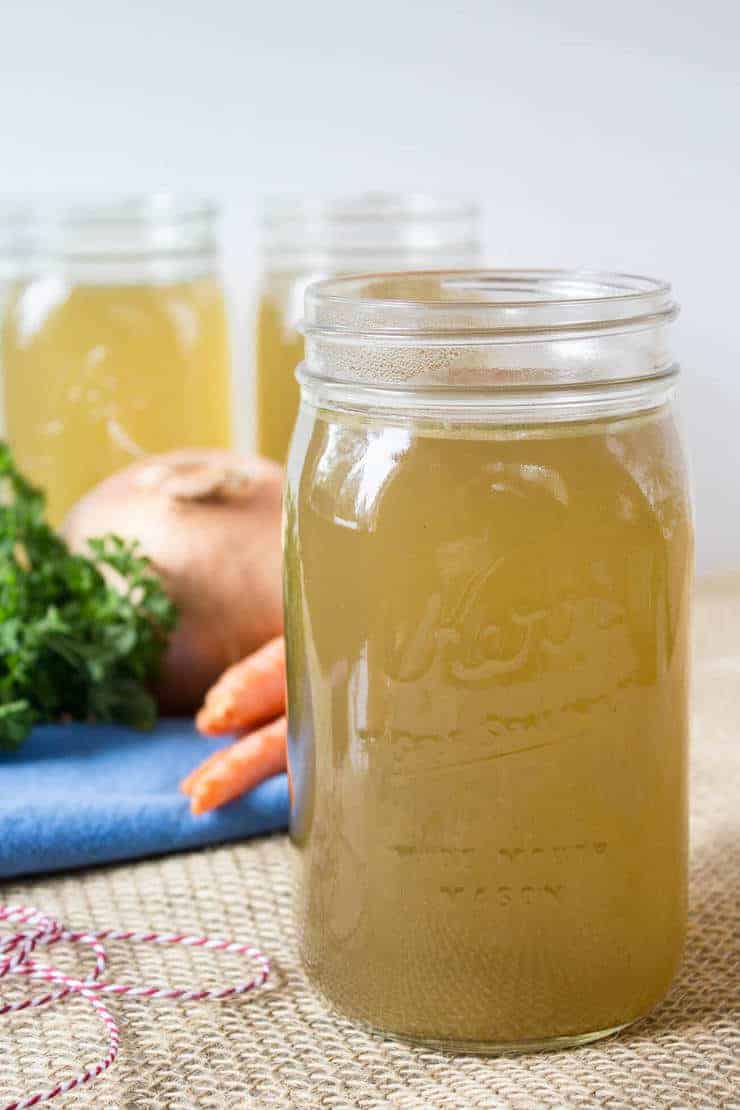 Homemade Chicken Broth in a glass jar with fresh vegetables in the background.