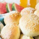 A basket full of hamburger buns with sesame seeds.