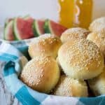 A basket lined with a blue and white napkin filled with sesame seed hamburger buns.