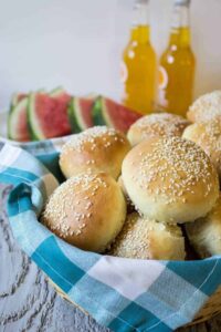 A basket lined with a blue and white napkin filled with sesame seed hamburger buns.