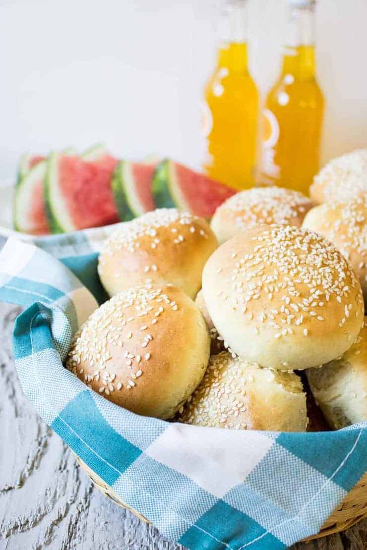 A basket full of rolls with wedges of watermelon and orange soda behind the basket. 