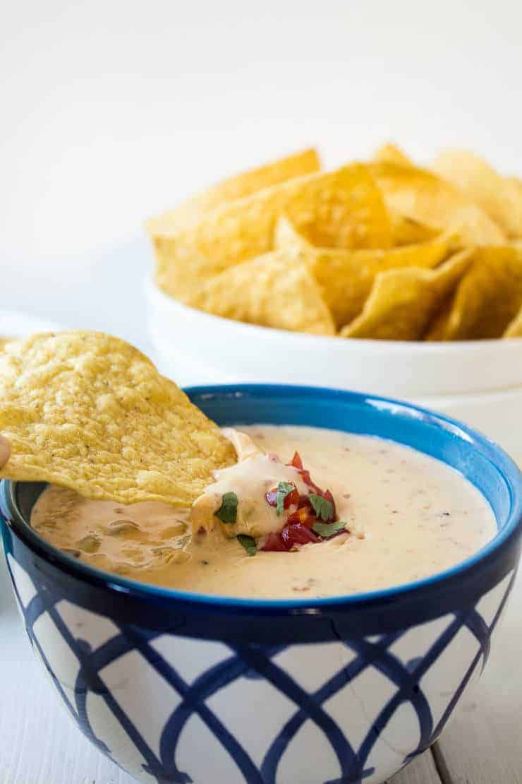 A corn chip dipping into a bowl of creamy cheese sauce.