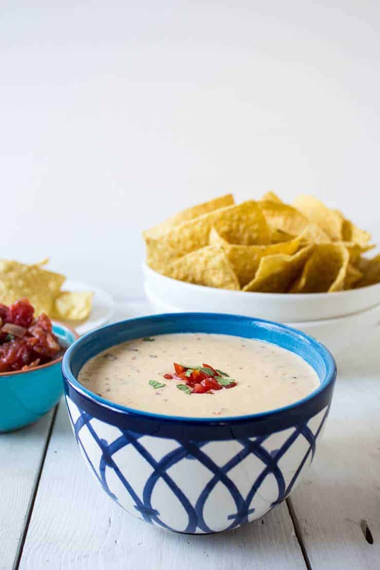 Mexican Cheese Dip topped with fresh tomatoes and cilantro in a blue and white bowl.