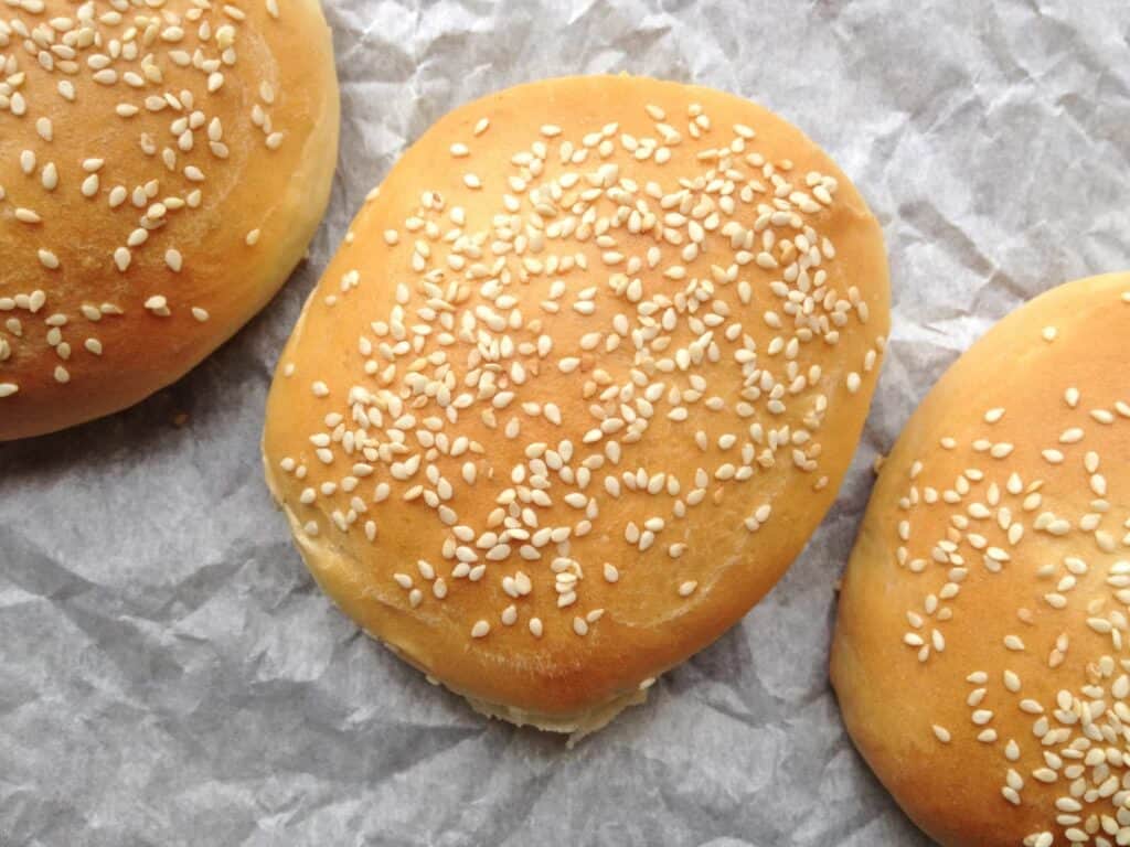 Three hamburger buns topped with white sesame seeds. 