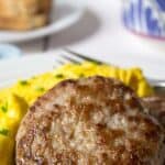 Meat patty and scrambled eggs on a white plate.