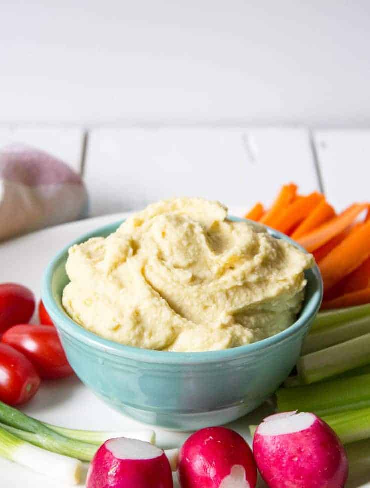 A bowlful of hummus with fresh veggies surrounding the bowl. 