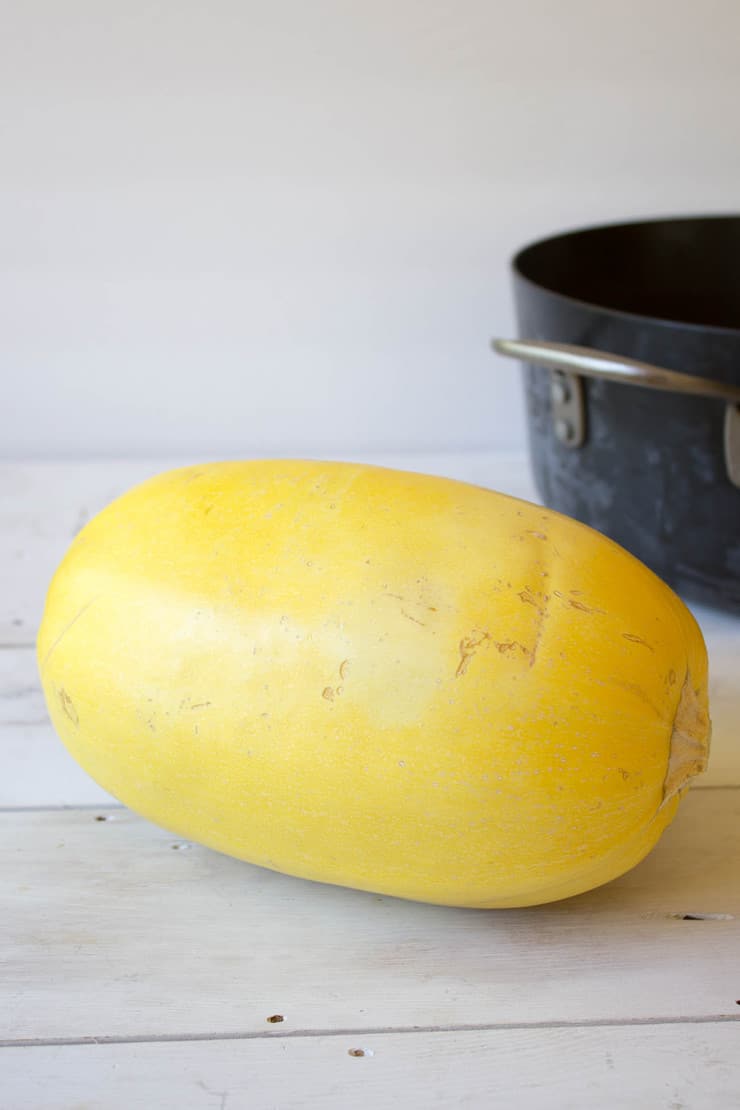 A whole Spaghetti Squash next to a black pot.