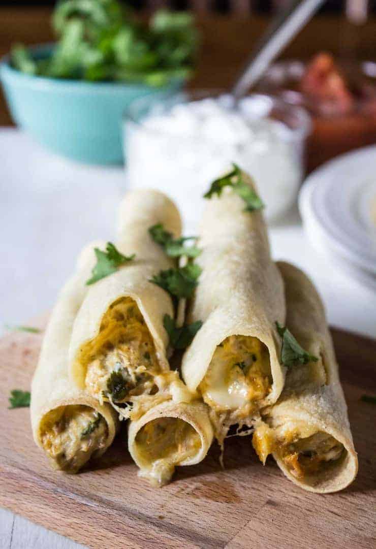 Baked Chicken Taquitos stacked on a wooden board and topped with cilantro.