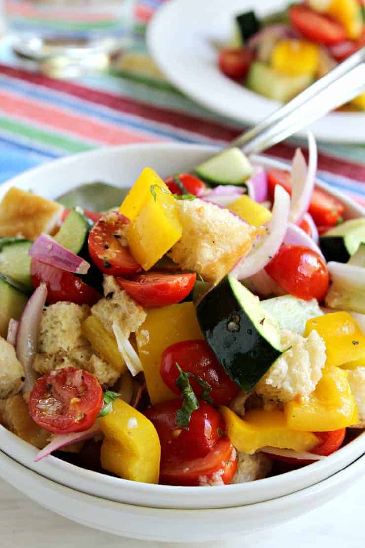 Cucumbers, bell peppers, tomatoes and onions in a white bowl.