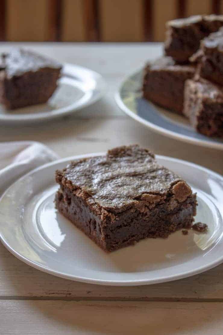 A single brownie on a plate with a plate of brownies in the background.