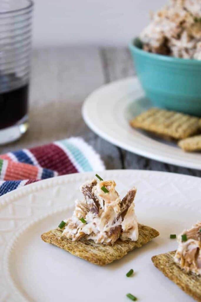 A white plate with crackers topped with a cheese spread.