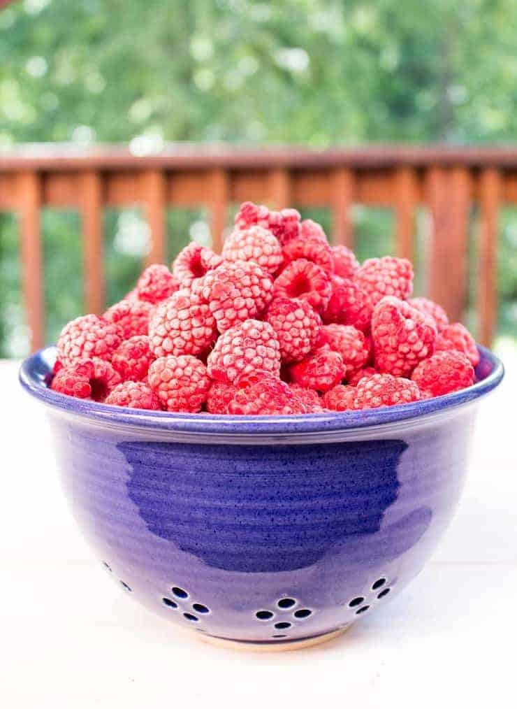 A blue colander filled with frozen raspberries.