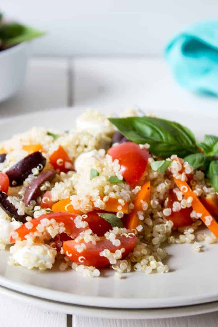 Quinoa, bell peppers, olives, mozzarella in a salad on a white plate.