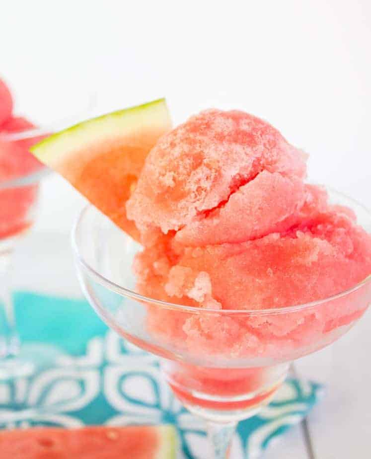 A glass dish filled with watermelon sorbet and garnished with a watermelon slice. 
