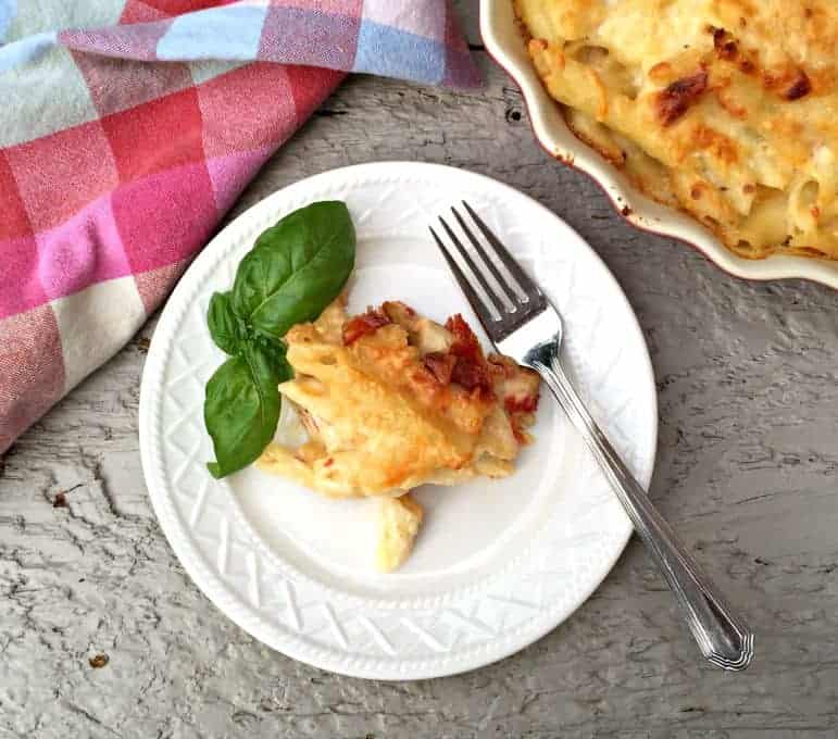 Baked Cheesy Penne on a small white plate with a fresh sprig of basil.