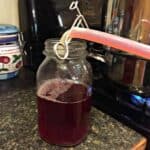 Pouring hot plum juice from a tube into a glass jar.