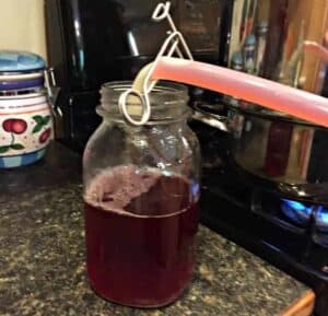 Pouring hot plum juice from a tube into a glass jar.