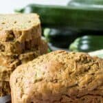 A loaf of zucchini bread with fresh zucchini behind the loaf of bread.
