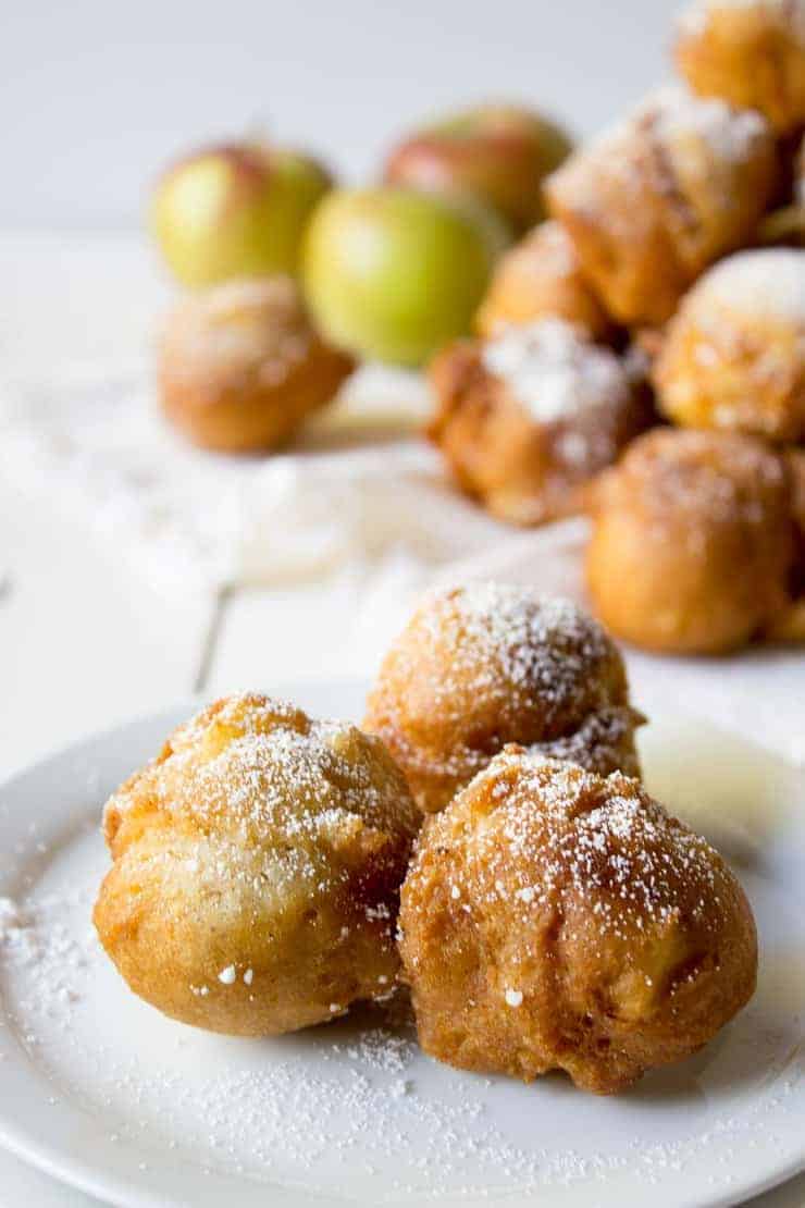 Three round fritters topped with powdered sugar on a small white plate.