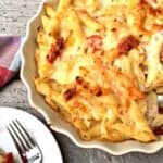Baked cheesy penne pasta with chicken and roasted tomatoes in a white baking dish.