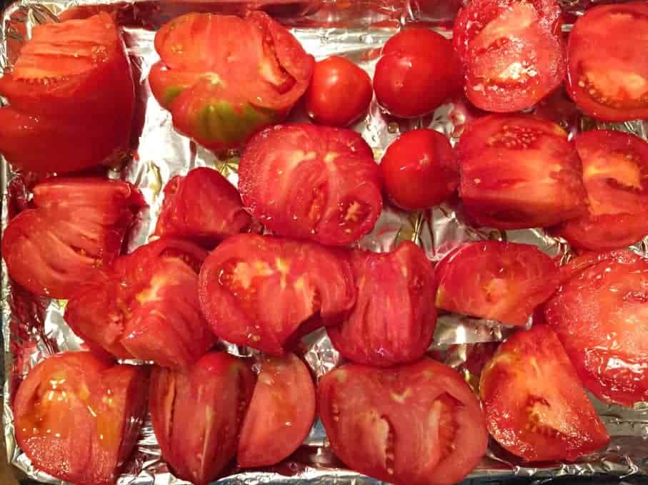 Tomatoes with olive oil on a foil lined baking sheet.