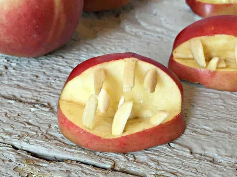 A red skinned apple cut into a wedge shaped mouth with almonds sticking out as teeth.