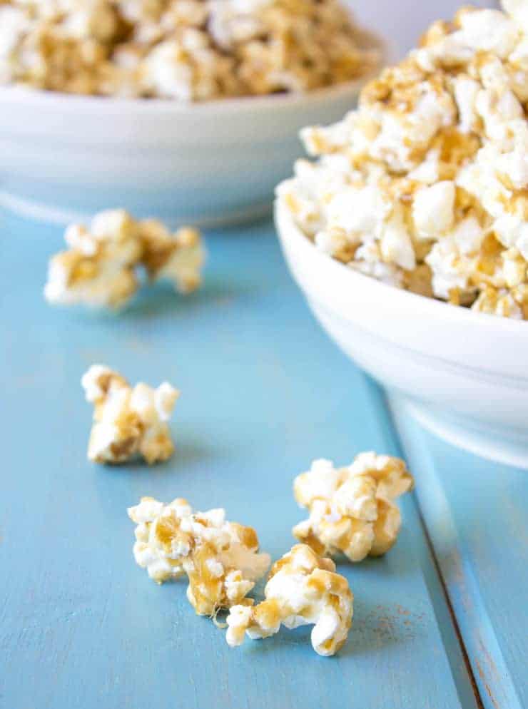 Caramel Popcorn in white bowls with a few pieces sprinkled on a turquoise board.