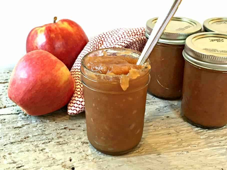 Apple butter in glass canning jars next to two red apples.