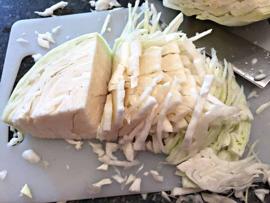 Green cabbage on a cutting board sliced into long strips. 