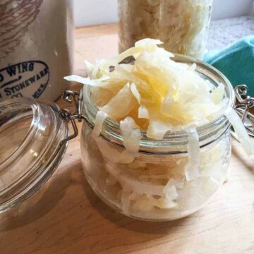 A glass crock overfilling with sauerkraut.