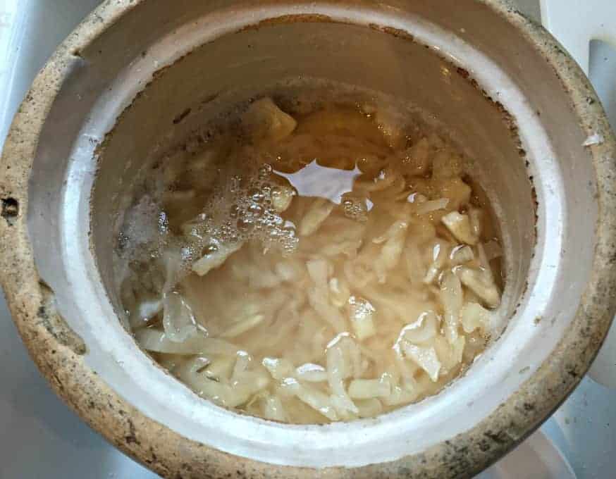 Looking down into an old crock filled with liquid and shredded cabbage.