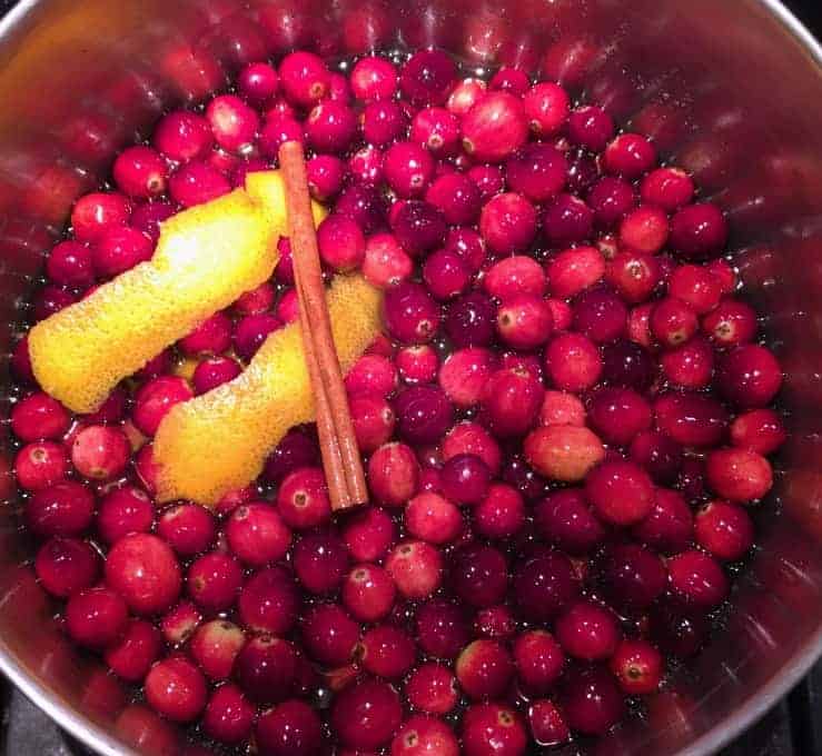 Whole cranberries in a pot along with orange peel and a cinnamon stick.