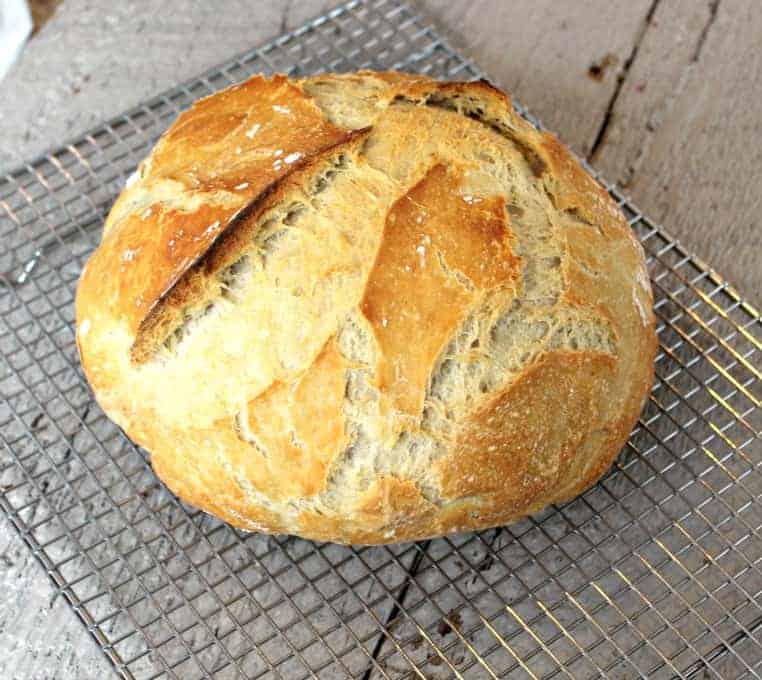 A round loaf of bread with cracks on the surface of the bread on a baking rack.