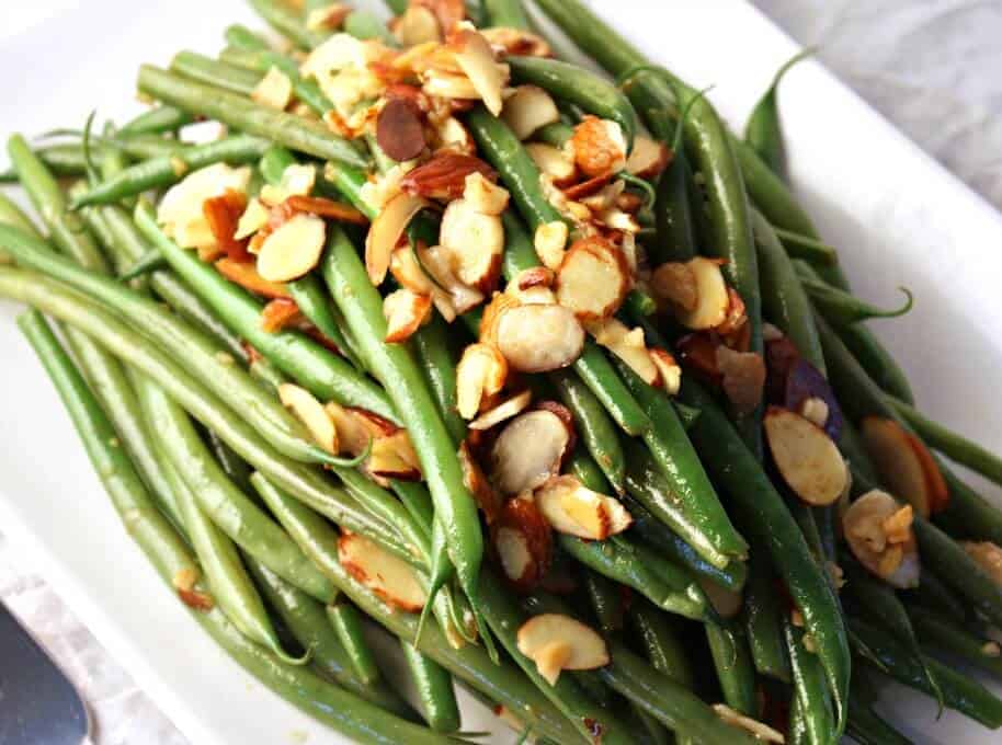 Fresh green beans with almonds served on a white plate.