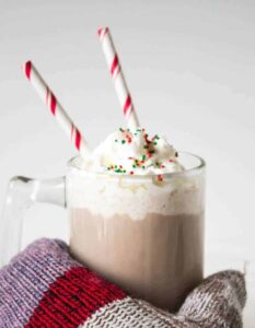 A glass mug filled with hot chocolate and whipped cream with two red and white straws in the glass.