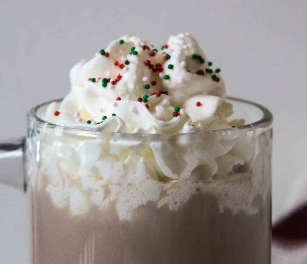 Whipped cream topped with colored sprinkles on a glass of chocolate milk.