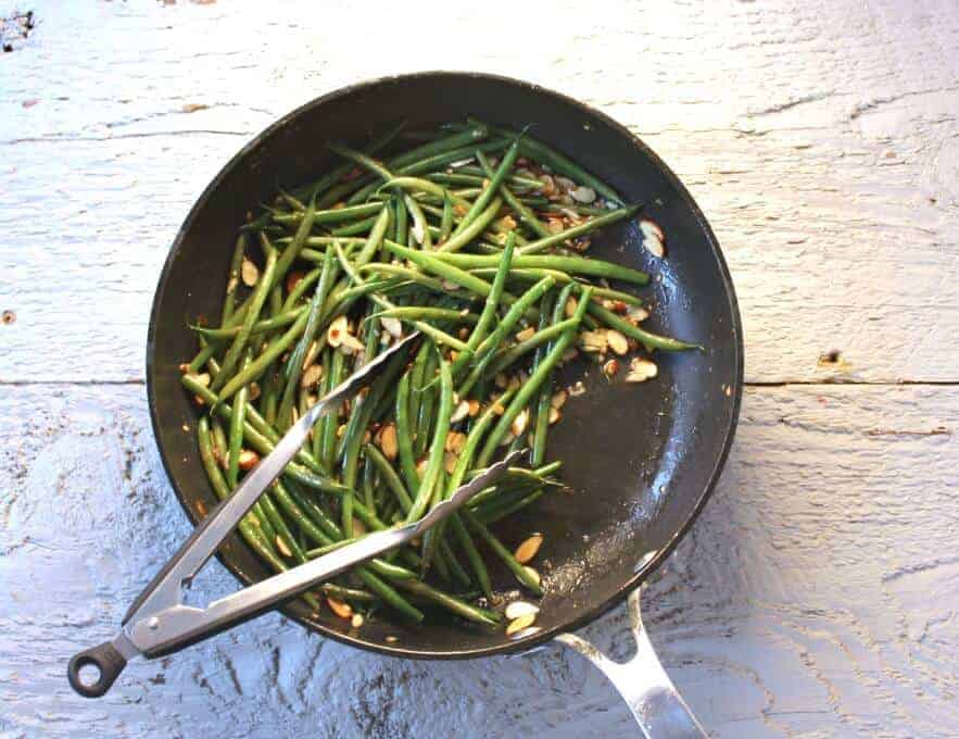 Green Bean Almondine in a skillet pan with a pair of tongs.