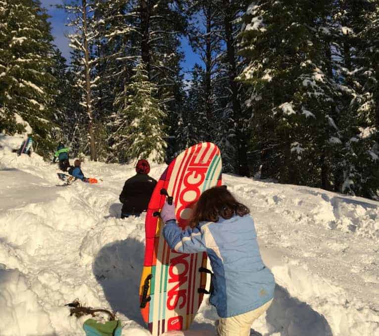 A girl in a blue jacket carrying a sled up a hill covered in snow.