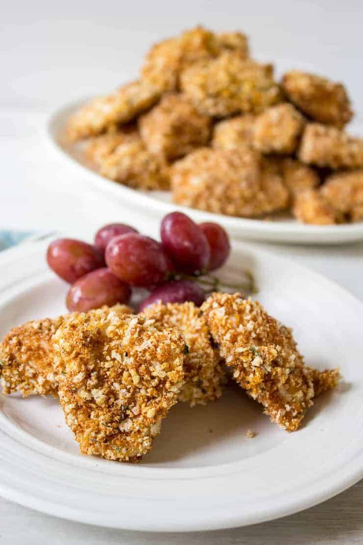 Baked chicken nuggets on a plate with red grapes.