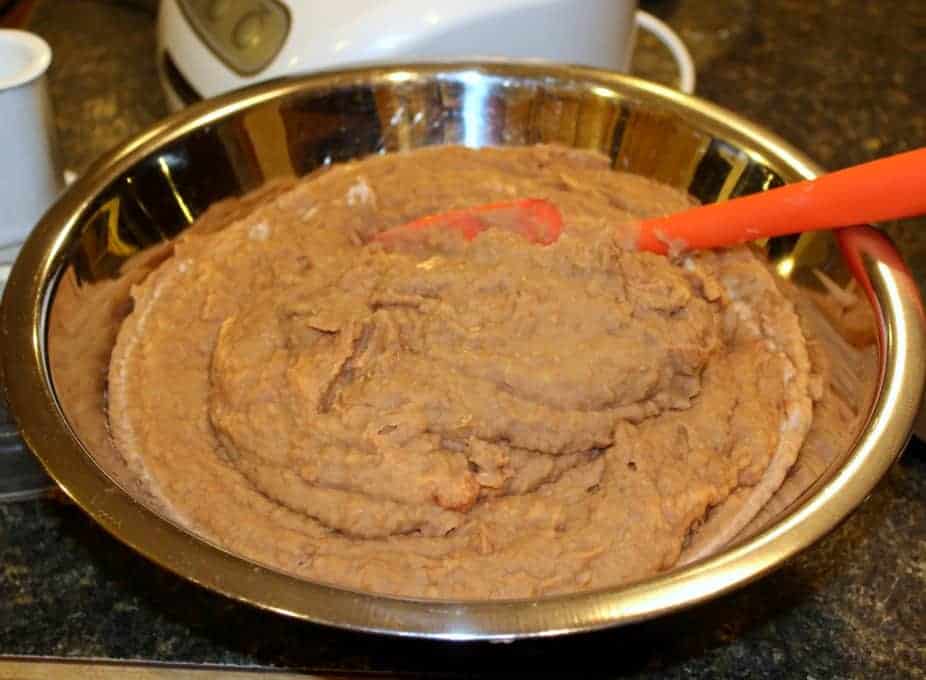 Huge metal bowl of refried beans with an orange spatula.