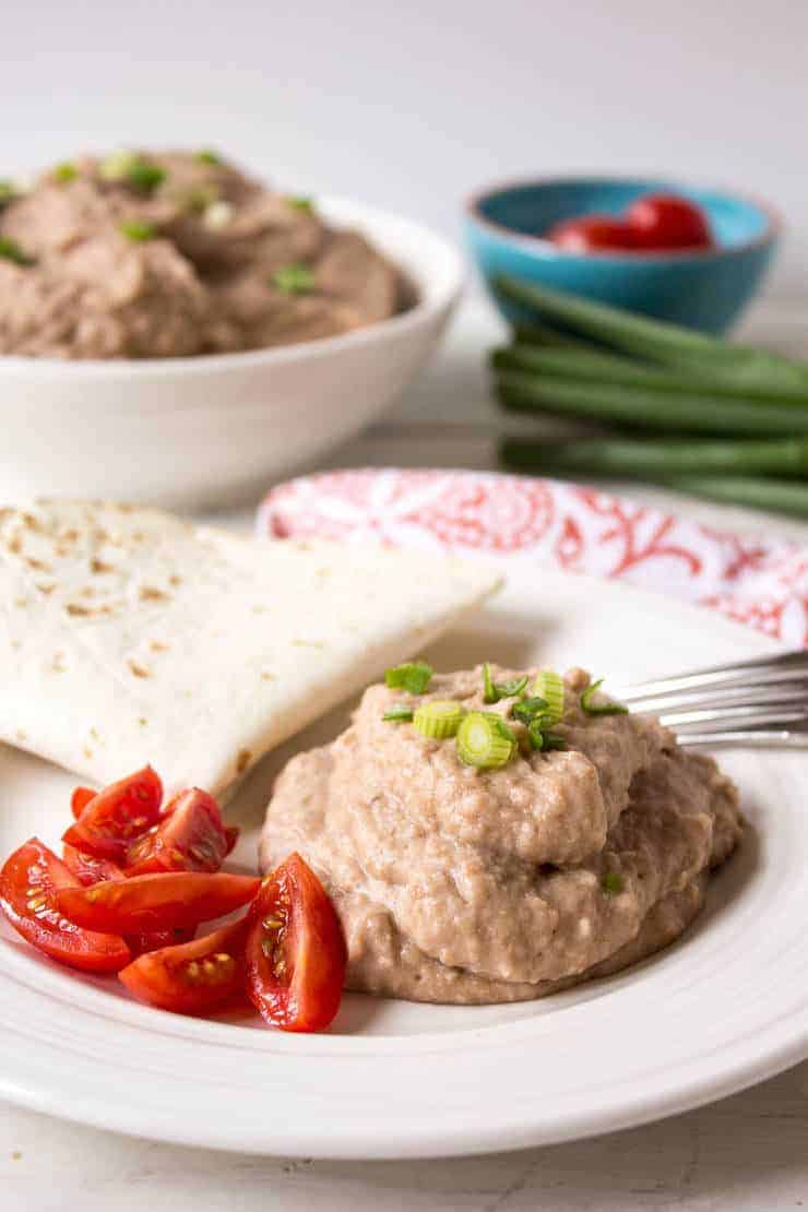 Beans topped with chopped green onions served with tortillas on a plate.