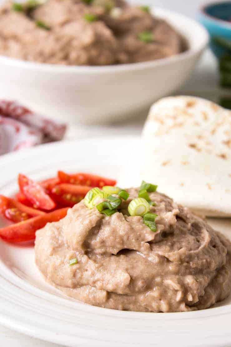 A white plate with beans, tomatoes and a tortilla.