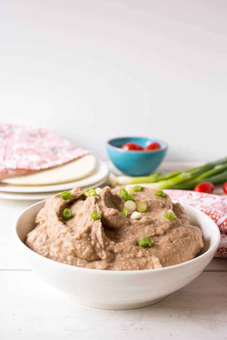 Crock Pot Refried Beans in a white bowl topped with chopped onions.