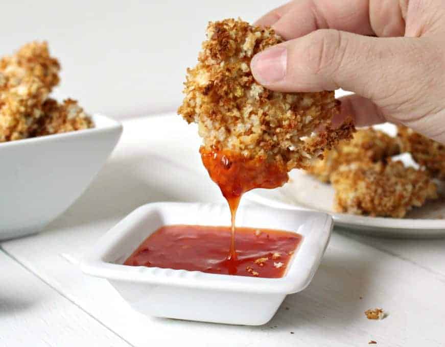 Baked chicken nugget being dipped into a sweet and sour sauce. 