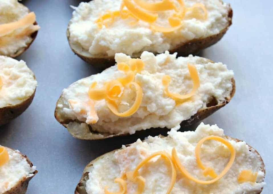 Twice Baked Potatoes topped with shredded cheese on a baking dish. 