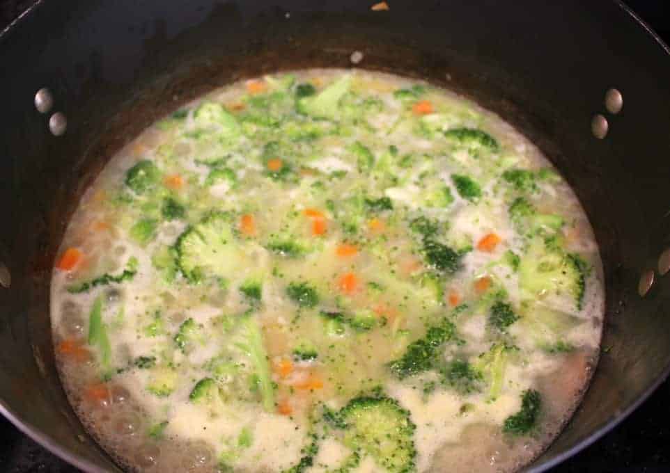 Broccoli, carrots and onions all cooking in a pot.