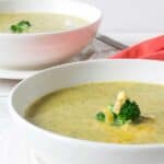 A bowl of creamy soup topped with shredded cheese and broccoli.