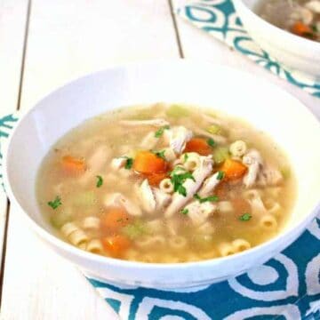 A white bowl filled with a clear broth with carrots, chicken and pasta.