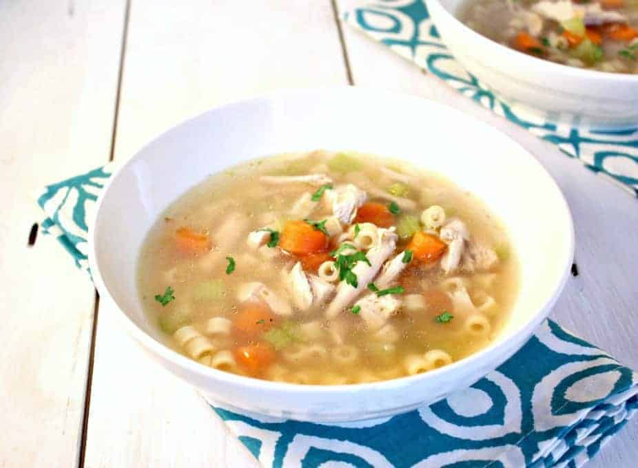 A white bowl filled with a clear broth with carrots, chicken and pasta.