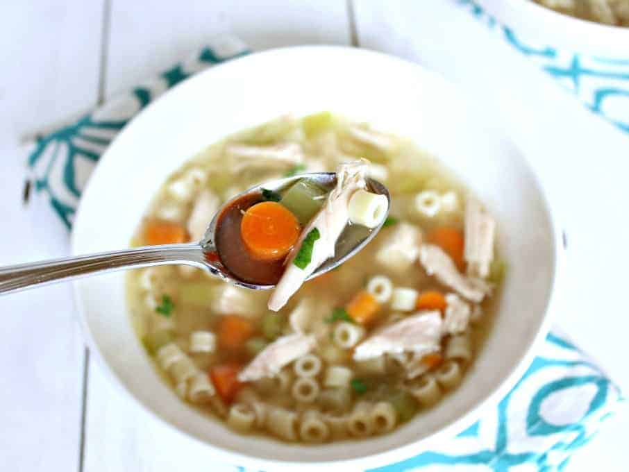 A spoonful of soup with carrots, celery, chicken and small pasta.